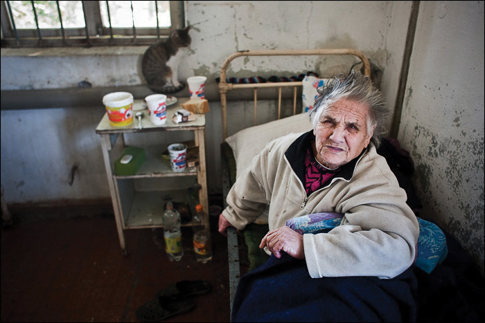 A person sitting in a dirty room with garbage strewn around.