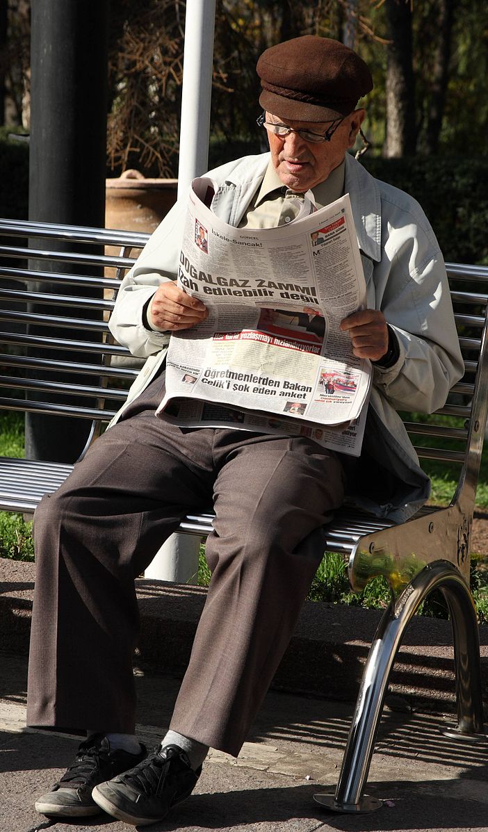 Man reading newspaper on park bench.
