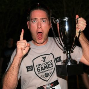 A European-American man celebrates as he holds a trophy he's won for winning a race.
