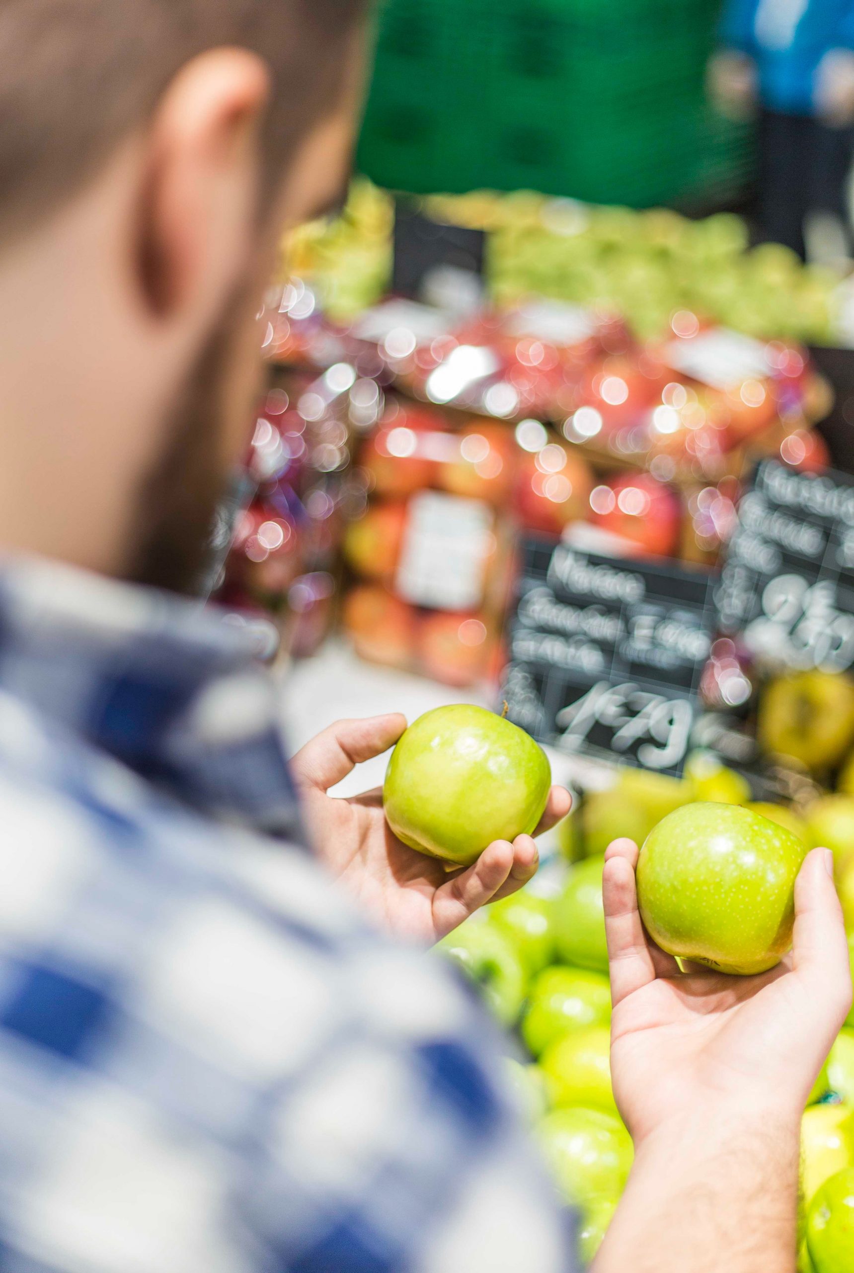 A man looking at two apples in the produce section of a store.