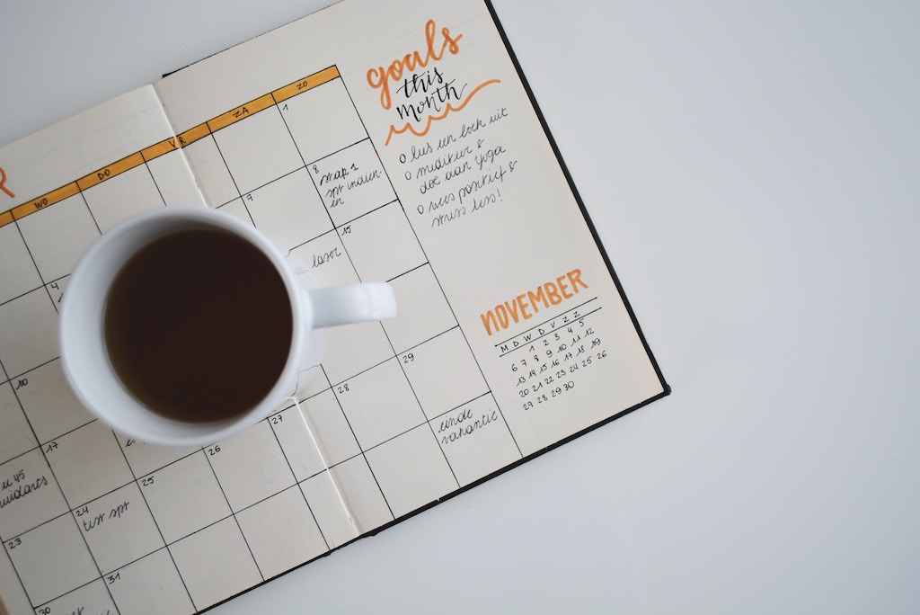 A photo of a coffee cup sitting on a calendar. The calendar has a section for goals this month.