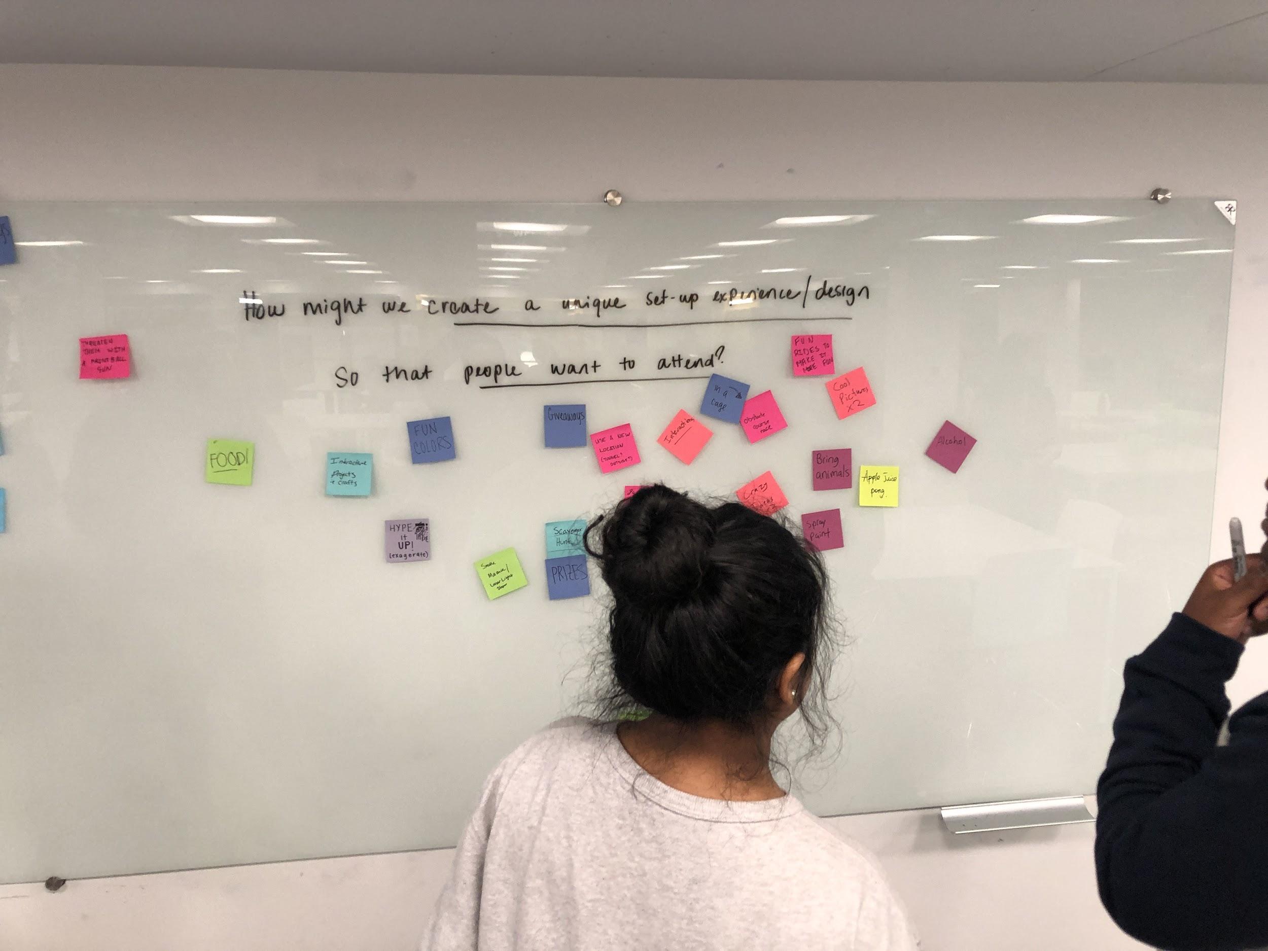 the back of two students staring at a whiteboard with bright sticky notes on it