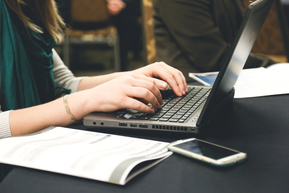 a person typing on a laptop with a magazine open on the side