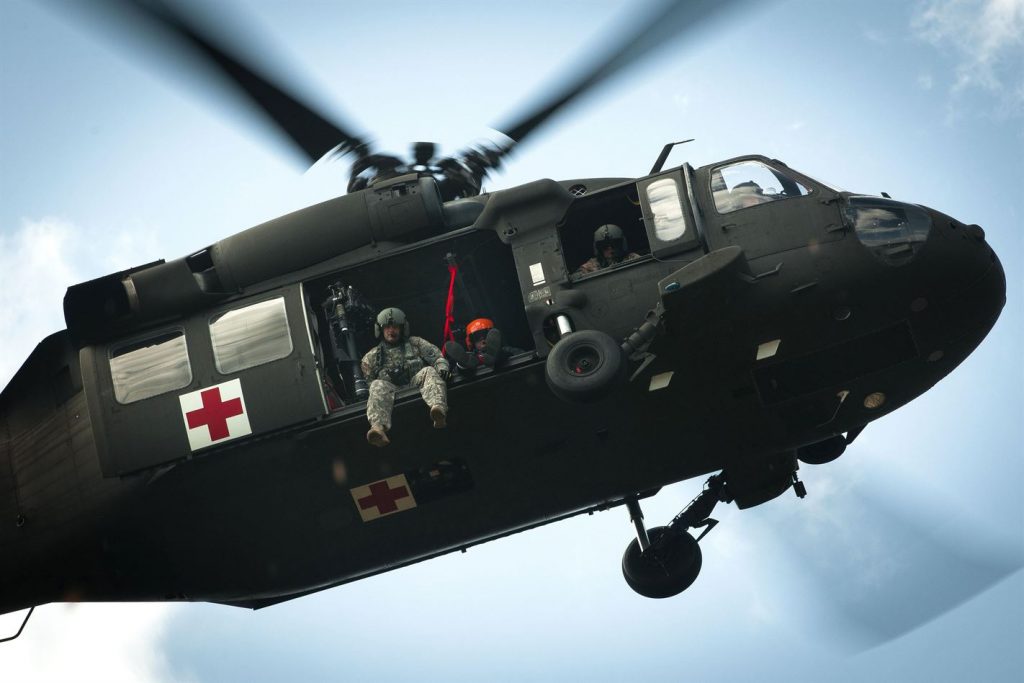 an army helicopter hovers overhead, with soldiers looking down at the camera