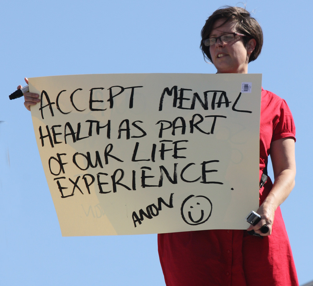 "One and Other-Mental Health" by Feggy Art is licensed under CC BY-NC-ND 2.0 Woman in red dress holding sign that says Accept Mental health as part of our life experience.