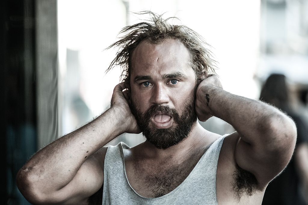“Homeless man in Los Angeles(7618018076).jpg” by Alex Proimos is licensed under CC BY 2.0 Photo of man with hands over ears an mouth open