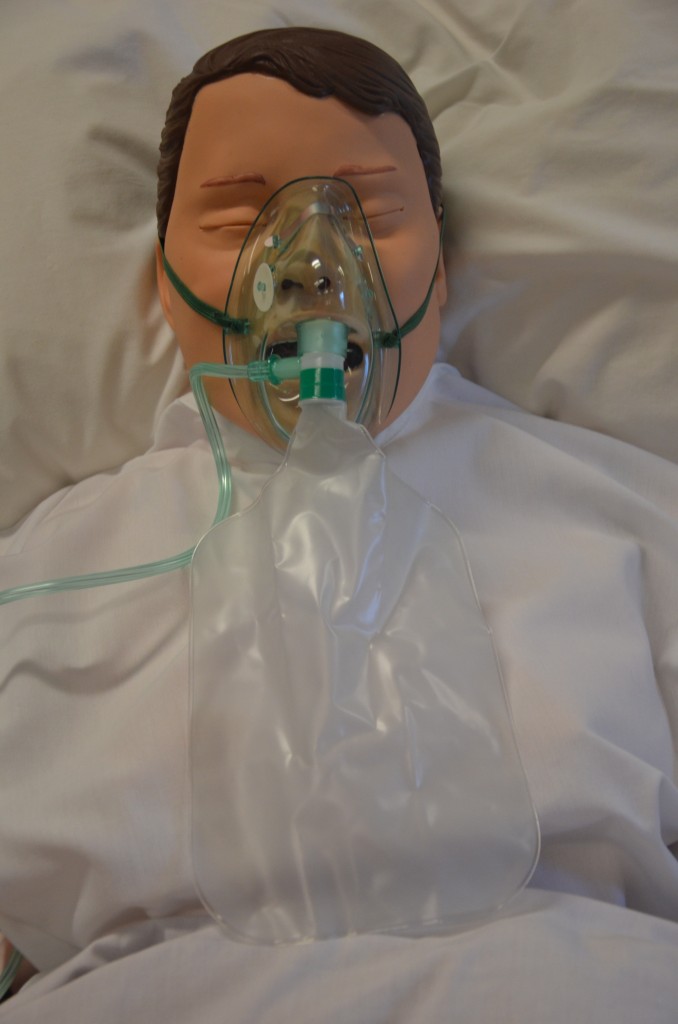 “DSC_2083.jpg” by British Columbia Institute of Technology (BCIT) is licensed under CC BY 4.0.. Access for free at https://opentextbc.ca/clinicalskills/chapter/5-5-oxygen-therapy-systems/ Photo showing a simulated patient wearing a non-rebreather mask
