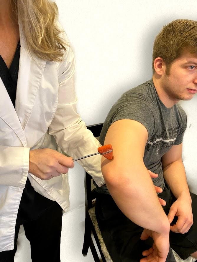 Deep Reflex Exam image 2.png" by Meredith Pomietlo for Chippewa Valley Technical College is licensed under CC BY 4.0 Photo showing nurse testing reflex on patient's tricep