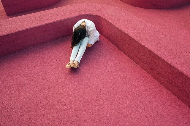 Girl curled over self in distress with pink background