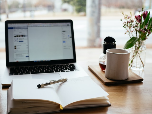 Journal and pen in front of laptop with coffee mug to the right