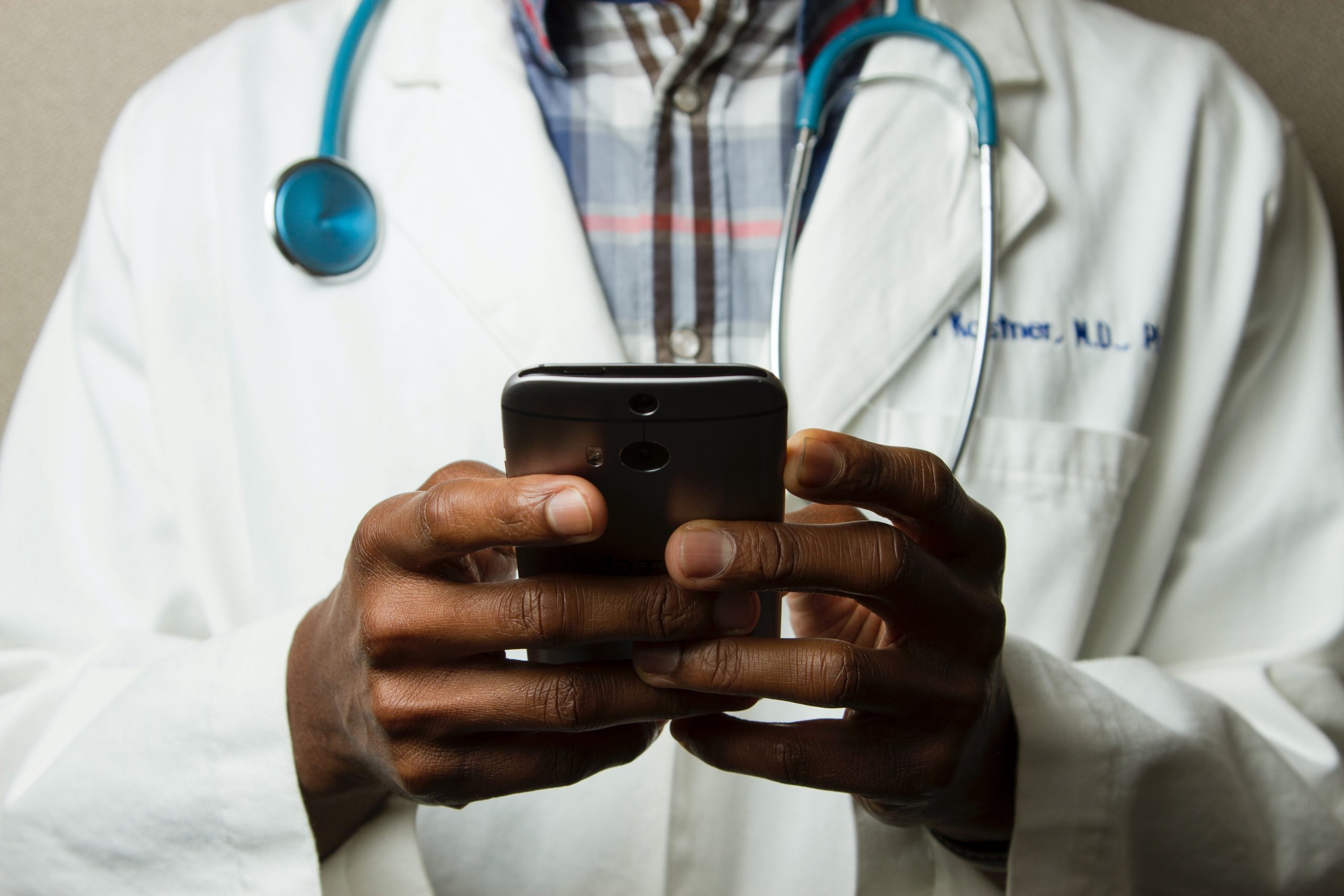 Doctor in lab coat and stethoscope holding cell phone.