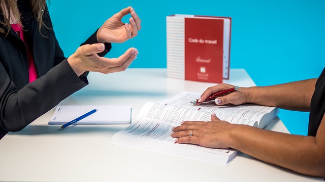 Arms of two persons sitting at a table with notebook, book and pens