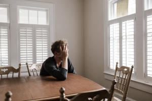 Man sitting at dining room table with his head in his hands.