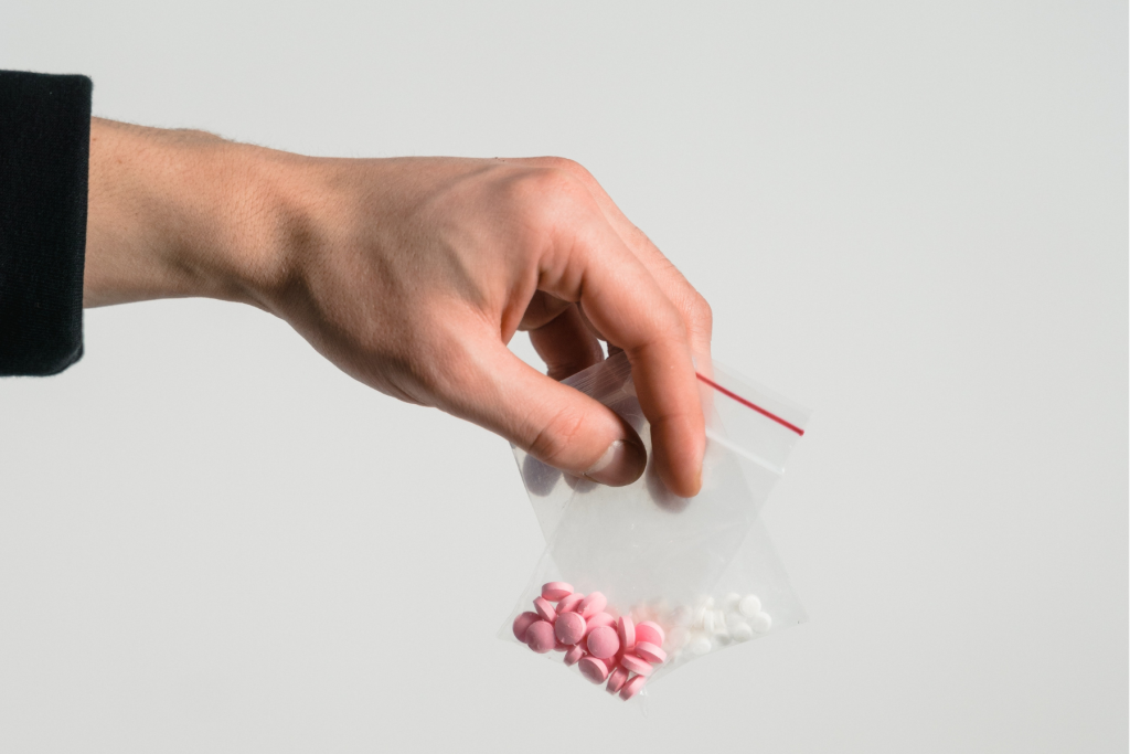 Hand reaching out holding two baggies of small pills.