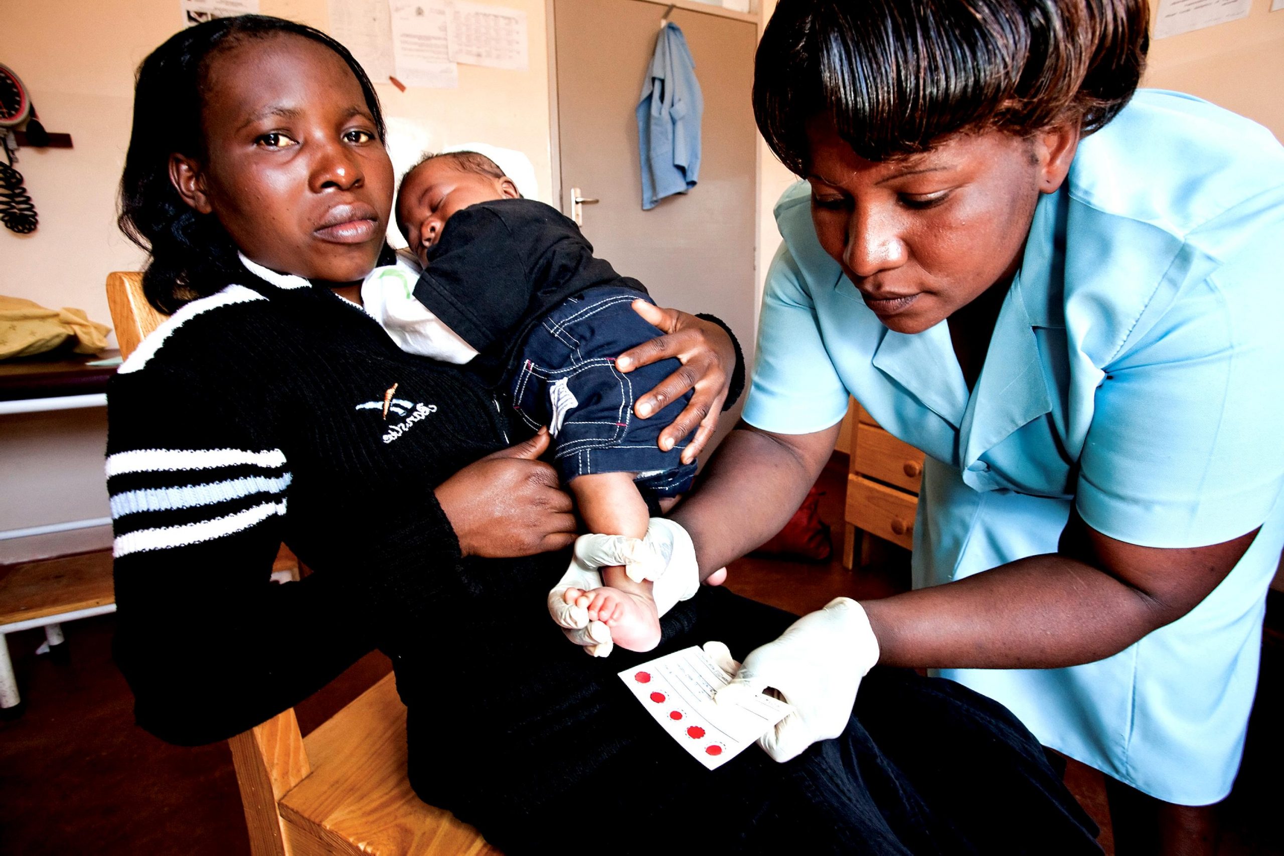 ”PIXNIO-45563-3000x2000” by by USAID on Pixnio is licensed under CC0 Photo showing a seated mother holding an infant while a nurse performs health screenings on the infant