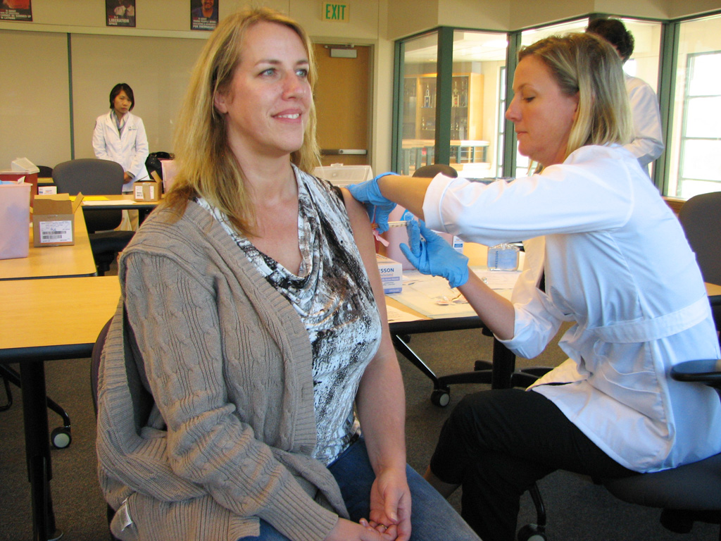 ”10442934136_1f910af332_b” by Lower Columbia College (LCC) is licensed under CC BY_NC-ND 2.0 Photo showing a smiling woman receiving a vaccination from a gloved medical provider