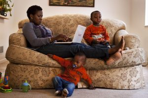 Mother and two sons at a couch. The mother is on a computer.