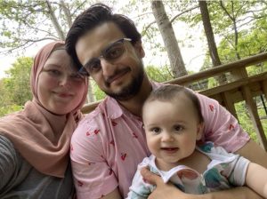 A mother, father, and child sitting on a deck with trees in the background.